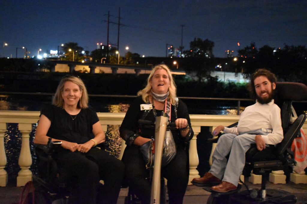Three people sitting on a balcony by the water.